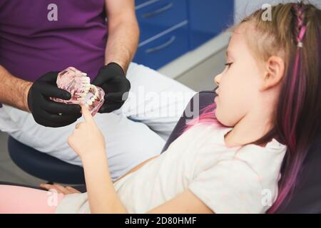 Der Zahnarzt erzählt dem Kind von der Mundhygiene und zeigt einen künstlichen Kiefer und eine Zahnbürste. Nahaufnahme Stockfoto