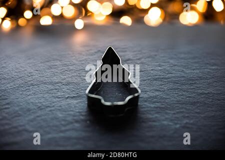 Weihnachtsbaum Plätzchen Cutter auf einem Schiefer vor weihnachten Lichter liegen. Selektiver Fokus Stockfoto