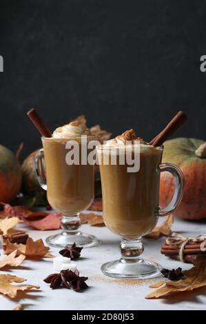 Zwei Glas-Tassen Kürbis Latte mit Gewürzen auf dunklem Hintergrund mit Kürbissen und Herbstblättern, Nahaufnahme Stockfoto