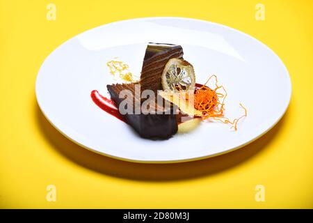 Luxus-Patisserie-Konzept. Stück Schokoladenkuchen mit vielen Schichten mit Sahne verbunden. Prager Schokoladenkuchen auf Teller auf gelbem Hintergrund. Köstliches Brownie-Gebäck im Café oder in der Bäckerei serviert. Stockfoto