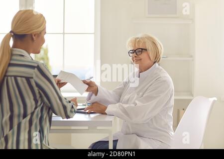 Freundliche ältere Ärztin gibt einem Patienten in seinem Büro ein Rezept. Stockfoto