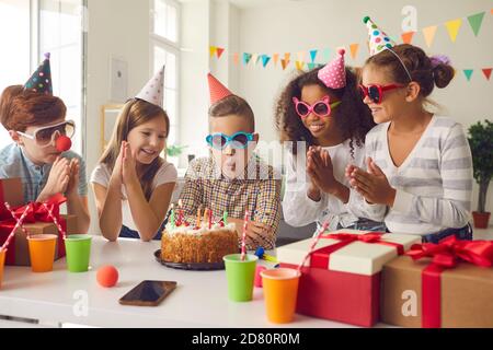 Geburtstagsjunge bläst Kerzen auf einem Kuchen zum Applaus Seiner multiethnischen Freunde bei seiner Partei zu Hause Stockfoto