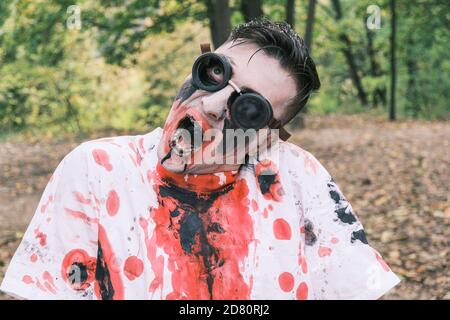 Horror, halloween und Zombie Konzept. Porträt eines unheimlichen Mannes mit Zombie Make-up mit Blutflecken und schwarzer Flüssigkeit im Mund wrigglert gegen Bac Stockfoto