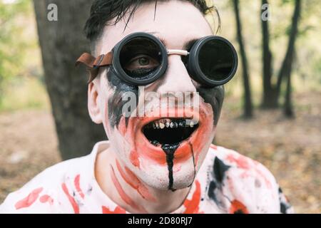 Horror, Halloween und Zombie Konzept. Portrait eines gruseligen Mannes in schwarzer Brille mit Zombie Make-up mit Blutflecken und schwarzer Flüssigkeit in seinem Mund Stockfoto