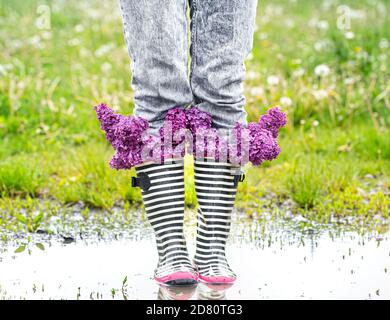 Kreativer Hintergrund. Eine junge Frau in Gummistiefeln mit Fliederblüten. Nahaufnahme. Stockfoto