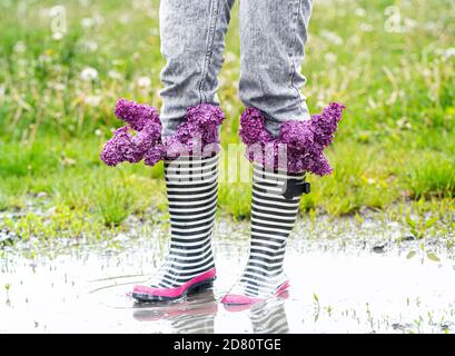 Kreativer Hintergrund. Eine junge Frau in Gummistiefeln mit Fliederblüten. Nahaufnahme. Stockfoto