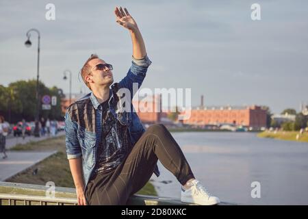 Der junge weiße Mann sitzt auf der Reise am Flussufer. Stockfoto