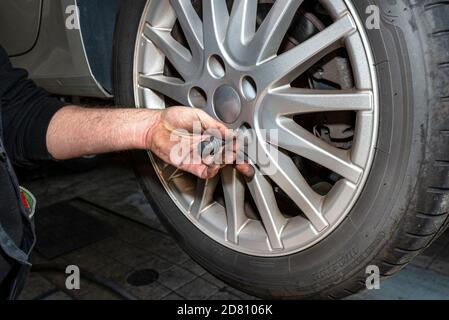 Der Automechaniker setzt die Schrauben ein, um die Aluminiumfelge des Autos an die Nabe zu Schrauben. Stockfoto