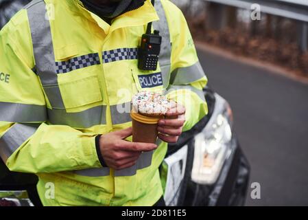 Männlicher Polizist in grüner Uniform, der eine Pause mit nimmt Donut auf der Straße Stockfoto