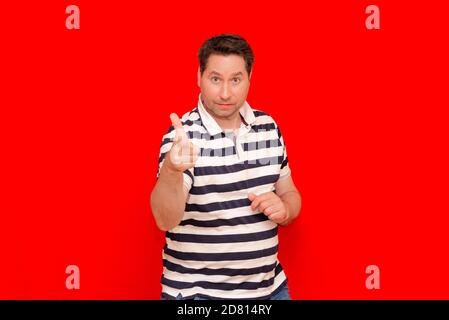 35s Mann trägt lässiges gestreiftes T-Shirt über isoliertem Rot stehen Die Wand zeigt und zeigt mit der Fingernummer nach oben Stockfoto
