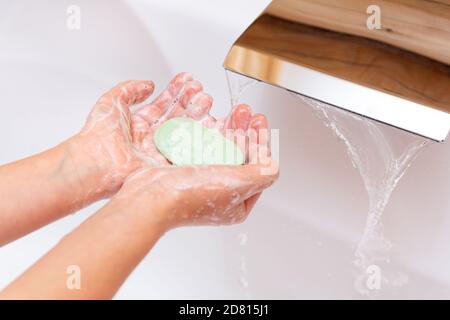 Das Kind wäscht seine Hände mit Seife unter einem Wasserhahn mit sauberem Wasser. Ein Stück grüne Seife in den Händen der Kinder Nahaufnahme. Hygienekonzept. Krankheit preven Stockfoto