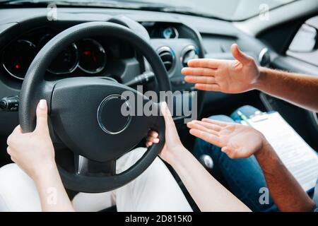 Weibliche Hände halten das Lenkrad. Männlicher Ausbilder zeigt mit seiner Hand, was man mit einem Rad machen kann. Nahaufnahme einer Frau, die ein Auto fährt. Drivin Stockfoto