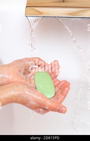 Das Kind wäscht seine Hände mit Seife unter einem Wasserhahn mit sauberem Wasser. Ein Stück grüne Seife in den Händen der Kinder Nahaufnahme. Hygienekonzept. Krankheit preven Stockfoto