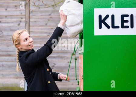 Frau, die alte oder gebrauchte Kleidung in den Spendenbehälter legt Stockfoto