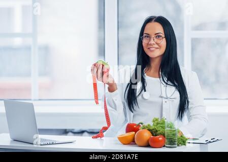 Ernährungsberaterin im weißen Mantel hält Apfel mit Maßband Stockfoto