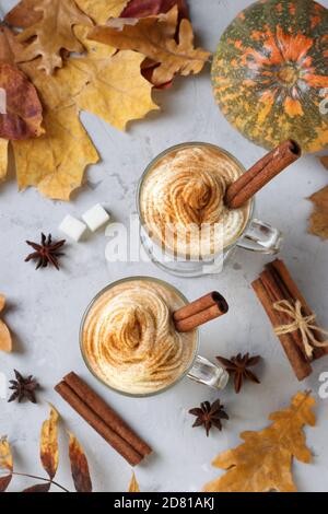 Zwei Glas-Tassen Kürbis Latte mit Gewürzen auf grauem Hintergrund mit Kürbissen und Herbstblättern. Blick von oben. Vertikales Format. Stockfoto