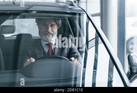 Happy stylish Senior Mann mit grauen Haaren und Schnurrbart ist Im modernen Auto Stockfoto