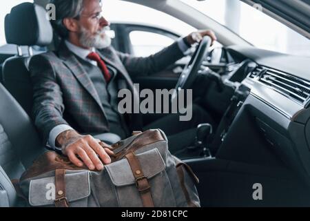 Modischer älterer Mann mit grauen Haaren und Schnurrbart im Urlaub Mit Tasche im Inneren modernen Automobil Stockfoto