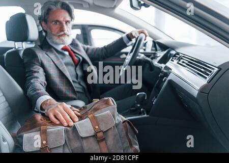 Modischer älterer Mann mit grauen Haaren und Schnurrbart im Urlaub Mit Tasche im Inneren modernen Automobil Stockfoto