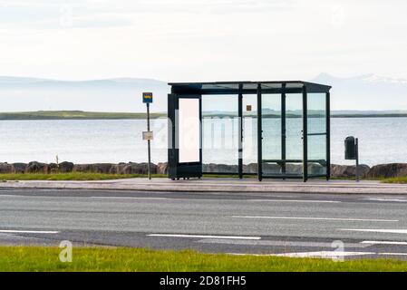 Einsame Bushaltestelle mit einem Unterstand mit einer leeren Plakatwand entlang einer Uferstraße. Ein A-Bay ist im Hintergrund sichtbar. Stockfoto