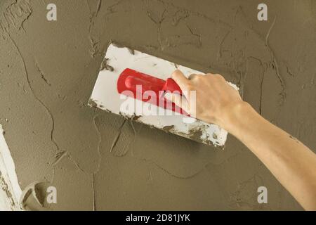 Der Arbeiter putzen die Wand mit dem Spachtel und trägt die Lösung des Zementmischers auf. Die Werkstatt legt den Putz auf die Trockenbauwand. Handwerker repariert Haus. Labor Stockfoto
