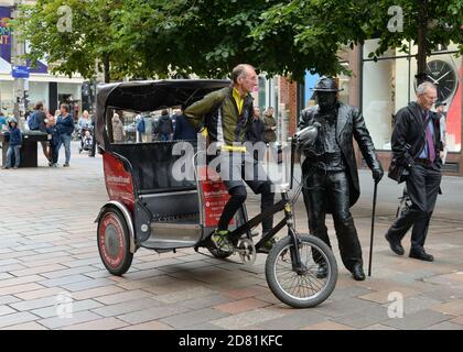 Ein Dreirad-Taxifahrer hält für ein Gespräch mit einem Menschen Statue Busker auf Buchanan Street, Glasgow, Schottland, Großbritannien Stockfoto