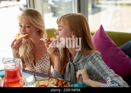 Zwei junge attraktive Frauen essen leckere Pizza im Café, haben Mahlzeit, leckeres Essen. Im leichten Café Stockfoto