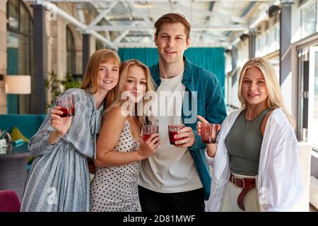 Porträt von vier kaukasischen Freunden mit Gläsern von Getränken posiert vor der Kamera im Café, Blick auf die Kamera und lächelt Stockfoto