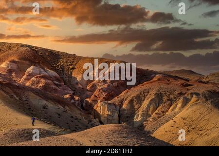 Hochwinkelaufnahme eines Touristen, der vor massiven roten Bergen im Kyzyl-Chin-Tal steht, auch Marstal genannt. Schöner wolkig Sonnenuntergang Himmel wie Stockfoto