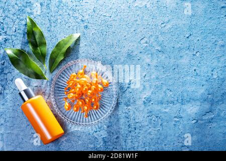 Bunte Komposition von Kosmetikprodukten mit orangen Baumblättern. Eine orangene Flasche Gesichtsserum und viele Vitamin C Konzentrat Kapseln auf einem Glas Stockfoto