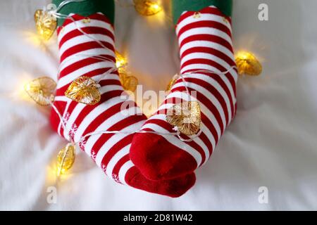 Weibliche Beine in Weihnachtssocken mit Girlande und festlichen Lichtern in Herzform. Konzept der romantischen Silvester Nacht, Elf Kostüm Stockfoto