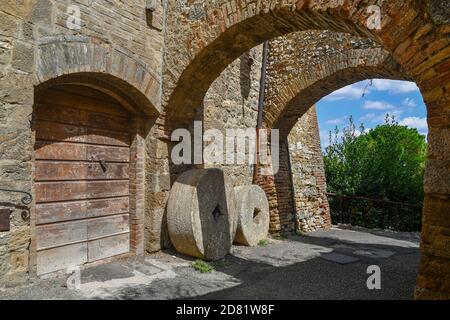 Blick auf eine gewölbte Gasse im mittelalterlichen Dorf mit alten Mühlsteinen an der Wand eines alten Hauses, San Gimignano, Siena, Toskana, Italien Stockfoto