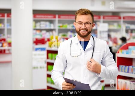 Junge kaukasische positive männliche Apotheker Arzt in weißen medizinischen Uniform mit digitalen Tablette und Stethoskop, Blick auf Kamera und Lächeln. Porträt Stockfoto