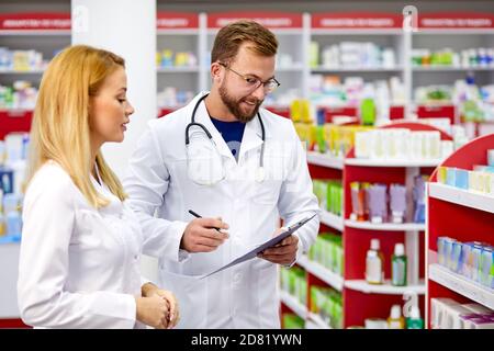 Team von jungen kaukasischen Chemikern oder Drogisten diskutieren Medikamente, überprüfen medizinische Indikationen, in weißen medizinischen Kittel, am Arbeitsplatz Stockfoto