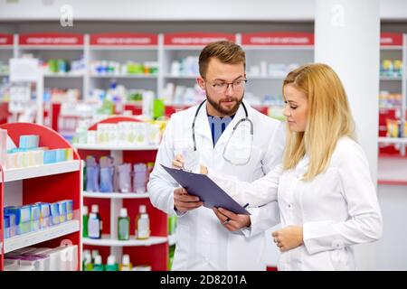 Zwei Apotheker Mann und Frau sprechen, diskutieren Medikamente. Professioneller Apotheker mit Praktikant in der modernen Apotheke, mit digitalen Tablette Stockfoto