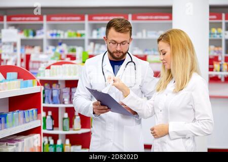 Zwei Apotheker Mann und Frau sprechen, diskutieren Medikamente. Professioneller Apotheker mit Praktikant in der modernen Apotheke, mit digitalen Tablette Stockfoto