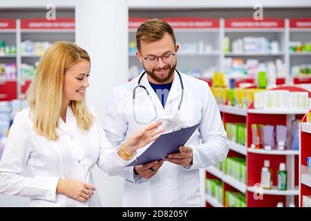 Team von jungen kaukasischen Chemikern oder Drogisten diskutieren Medikamente, überprüfen medizinische Indikationen, in weißen medizinischen Kittel, am Arbeitsplatz Stockfoto