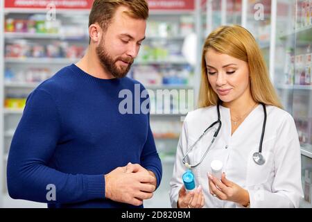 Junge weibliche Apotheke mit Droge und männliche Kunden in der Apotheke, Hilfe, Beratung. Medizin, Pharmazie, Gesundheitswesen und Menschen Konzept Stockfoto