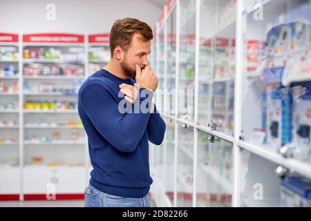 Junge kaukasischen erwachsenen Mann leidet an Halsschmerzen, brauchen einige Medikamente in der Apotheke Stockfoto