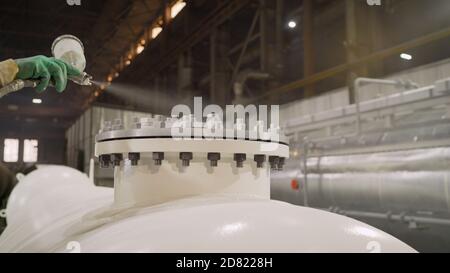 Lackieren von Teilen in einer metallverarbeitenden Fabrik. Arbeiter malt einen großen Teil in einer Fabrik. Stockfoto