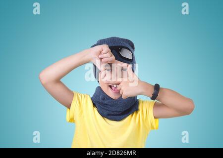 Ein Kind in einem gelben T-Shirt Hut und Schal wird auf einem helltürkisfarbenen Hintergrund fotografiert. Stockfoto