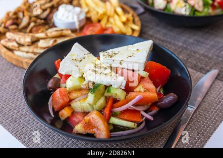 Gesunder griechischer Salat aus frischem Gemüse mit Tomaten, Pfeffer, Gurken, roten Zwiebeln, Oliven, Feta-Käse auf dem Tisch. Gesunde Ernährung, vegetar Stockfoto