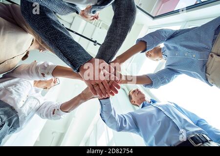 Überblick über Geschäftsleute, die ihre Hände zusammenlegen und Erfolge feiern, während sie im Büro stehen Stockfoto