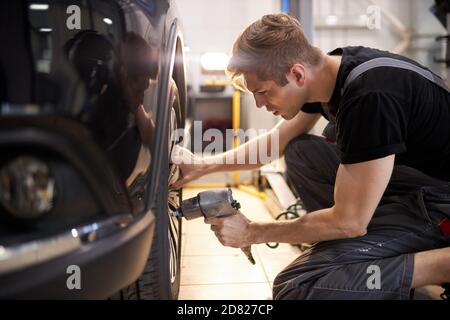 Konzentrierte professionelle Auto Mechaniker Mann Reparaturen ein Rad, das gebrochen hat, ändern Stockfoto