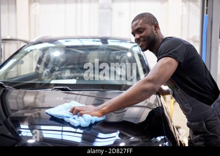 afro american Auto Mechaniker Mann wischt die perfekte Oberfläche der Maschine nach dem Polieren, die Vorbereitung eines Autos für den Besitzer nach der Reparatur Stockfoto