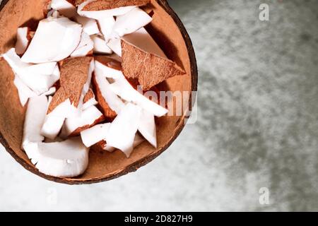 Eine Schüssel mit Kokosnussstücken auf Betongrund. Kokos-Zutat auf dem Teller. Veganer Bio-Snack in Zero Waste Kokosnussschale Stockfoto