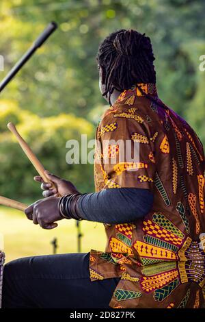 Rückansicht der jungen männlichen Performer mit Dreadlock Haar spielen Trommeln mit Stöcken während des Auftritten auf der Bühne während der Kulturfesta Im Park Stockfoto