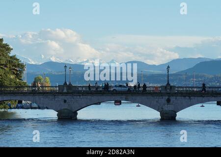 Quay Bridge in Zürich, Schweiz, mit Limmat im Vordergrund und Zürichsee und Alpen im Hintergrund. Es herrscht viel Verkehr. Stockfoto