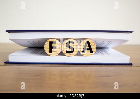 Konzept Wort "FSA, flexible Ausgaben Konto" auf hölzernen Kreisen zwischen den Seiten eines Buches auf einem schönen Holztisch. Weißer Hintergrund. Geschäftskonzept Stockfoto