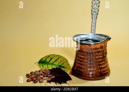 Gekochter türkischer Kaffee in traditioneller Kanne. Kaffeebohnen und geröstet gemahlener Kaffee mit gelb-grünem Blatt. Isolierter Hintergrund mit gelbem Hintergrund. Stockfoto